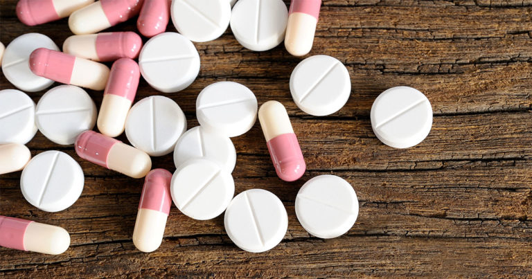 A collection of pills and pill capsules lying on a wooden surface.