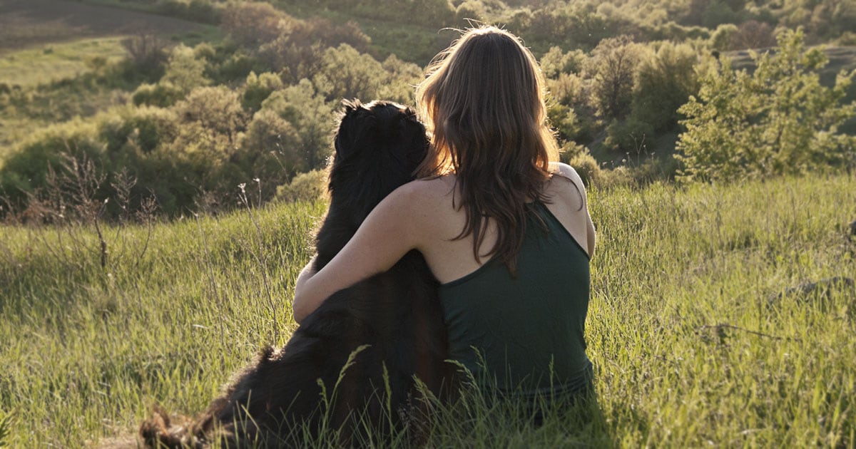 Woman and Black Dog Sitting on a Hill Overlooking a Forest | Diamond Pet Foods