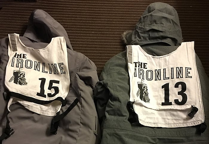Two winter coats lying face down with racing bibs attached to the back that read, 'The IronLine'.