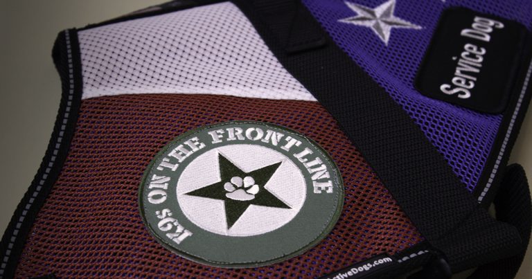 A close-up of a service dog's vest with a patch that reads, 'K9s on the front line'.