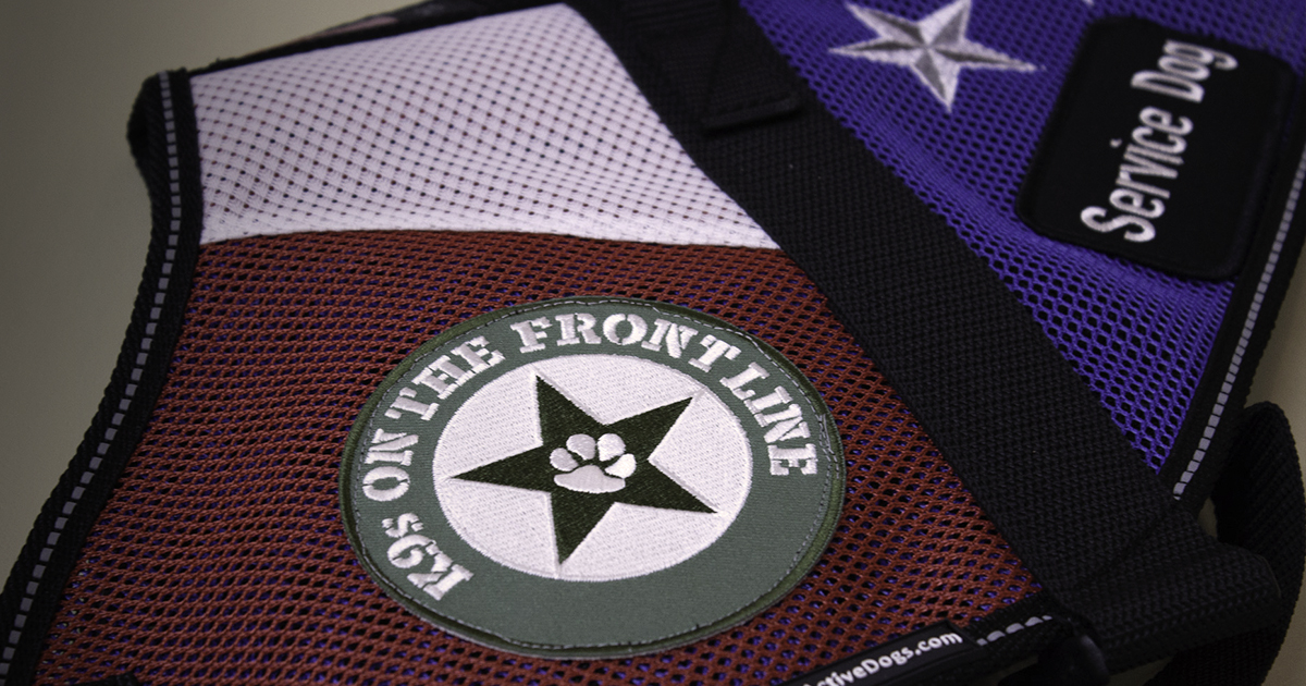 A close-up of a service dog's vest with a patch that reads, 'K9s on the front line'.
