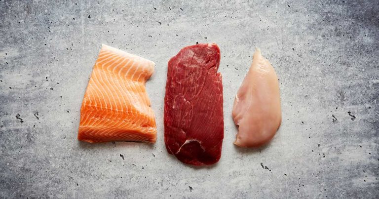 An overhead view of a cut of fish, beef and chicken lying side by side on a table.