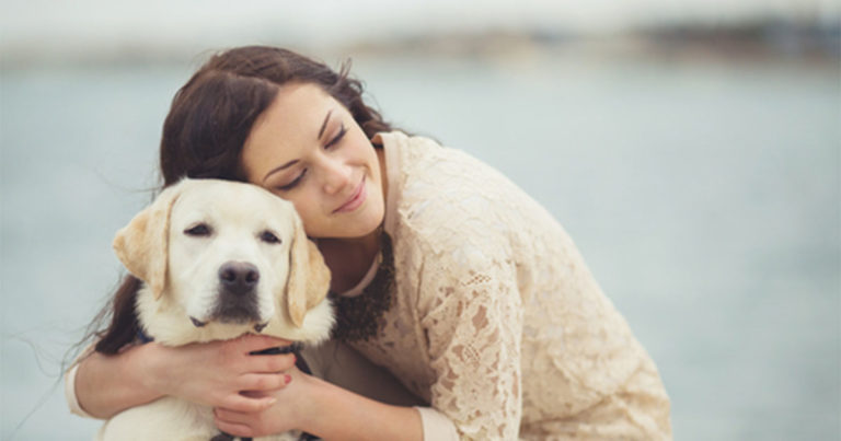 A woman bending down to hug her dog around the neck.