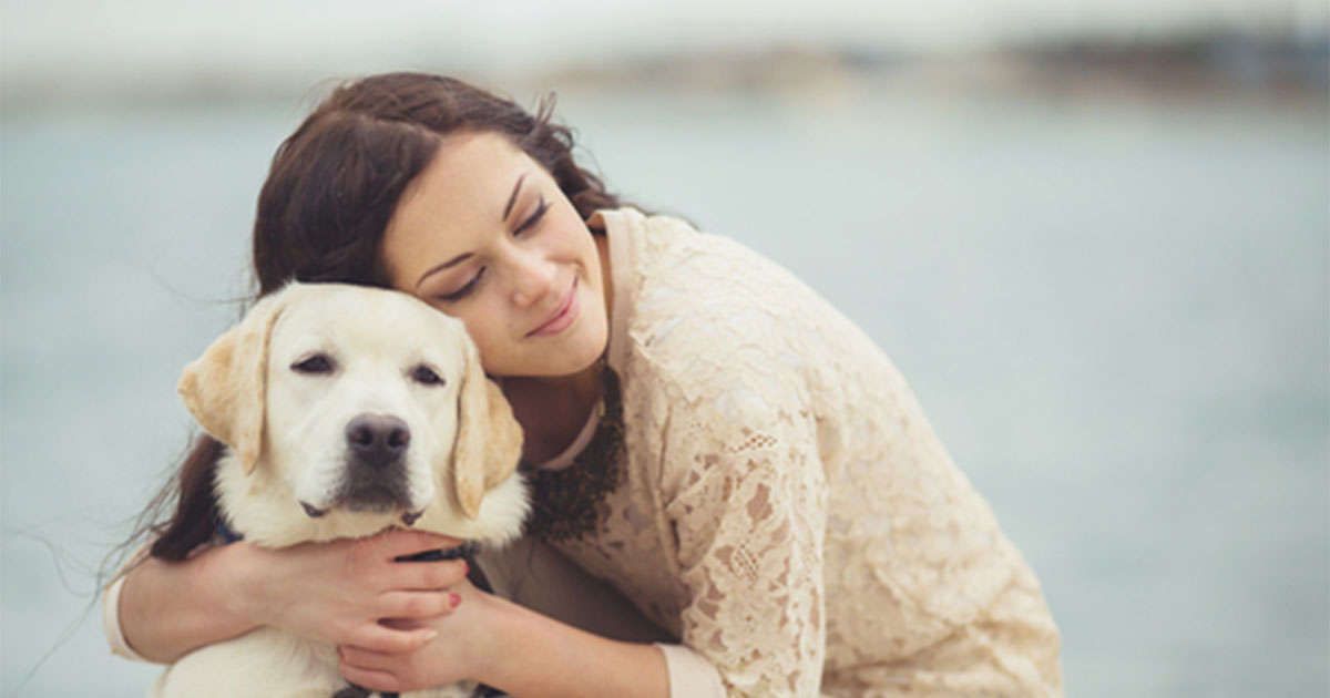 A woman bending down to hug her dog around the neck.