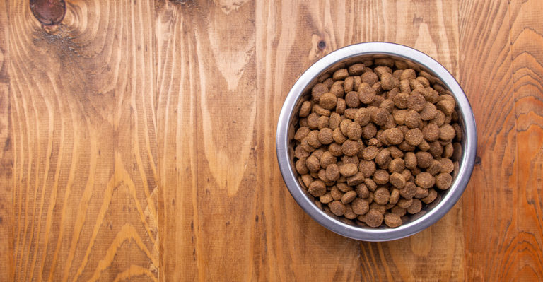 An overhead view of a metal bowl on a wooden table full of pet food.