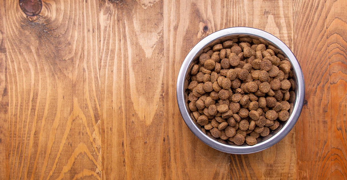 An overhead view of a metal bowl on a wooden table full of pet food.